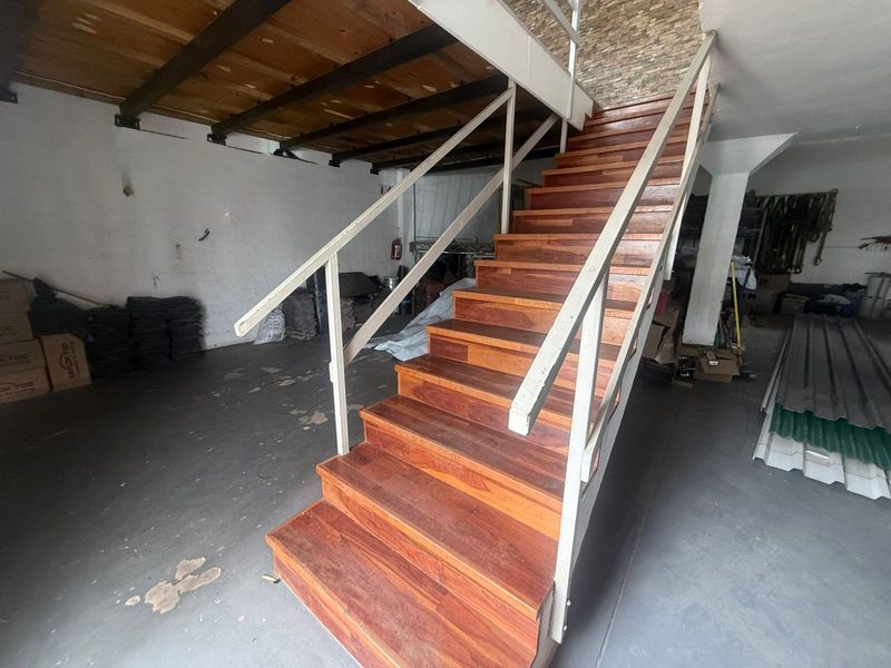 Industrial utility space featuring a prominent timber staircase with metal handrails, exposed ceiling beams, and a stone feature wall.