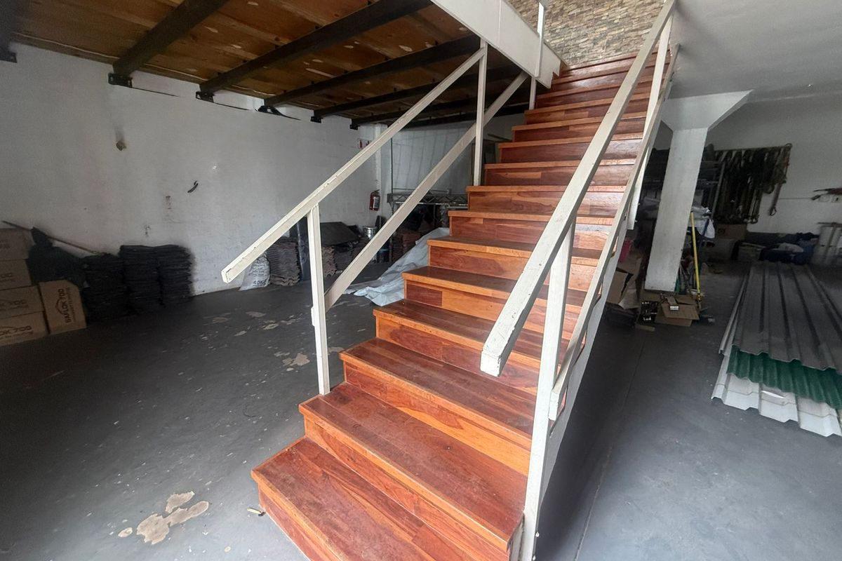 Industrial utility space featuring a prominent timber staircase with metal handrails, exposed ceiling beams, and a stone feature wall.