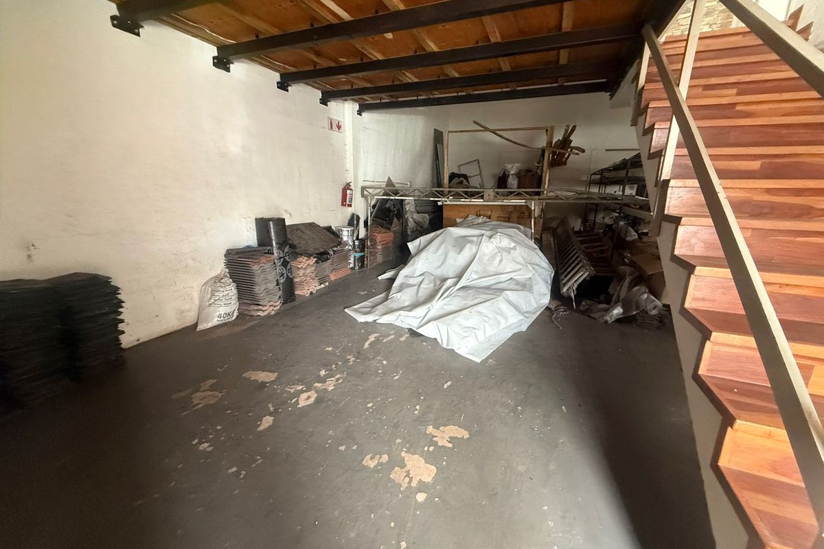 Industrial utility space featuring exposed timber ceiling beams, a wooden staircase, and concrete flooring, suitable for storage or workshop use.