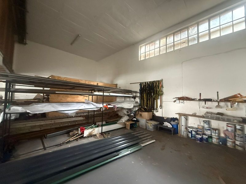 Industrial utility space featuring high-level clerestory windows, concrete flooring, and built-in wall shelving, suitable for storage or workshop use.