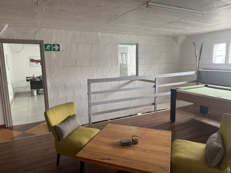 Industrial-style mezzanine living area featuring exposed concrete ceilings, painted blockwork walls, and laminate flooring with an adjacent office space.