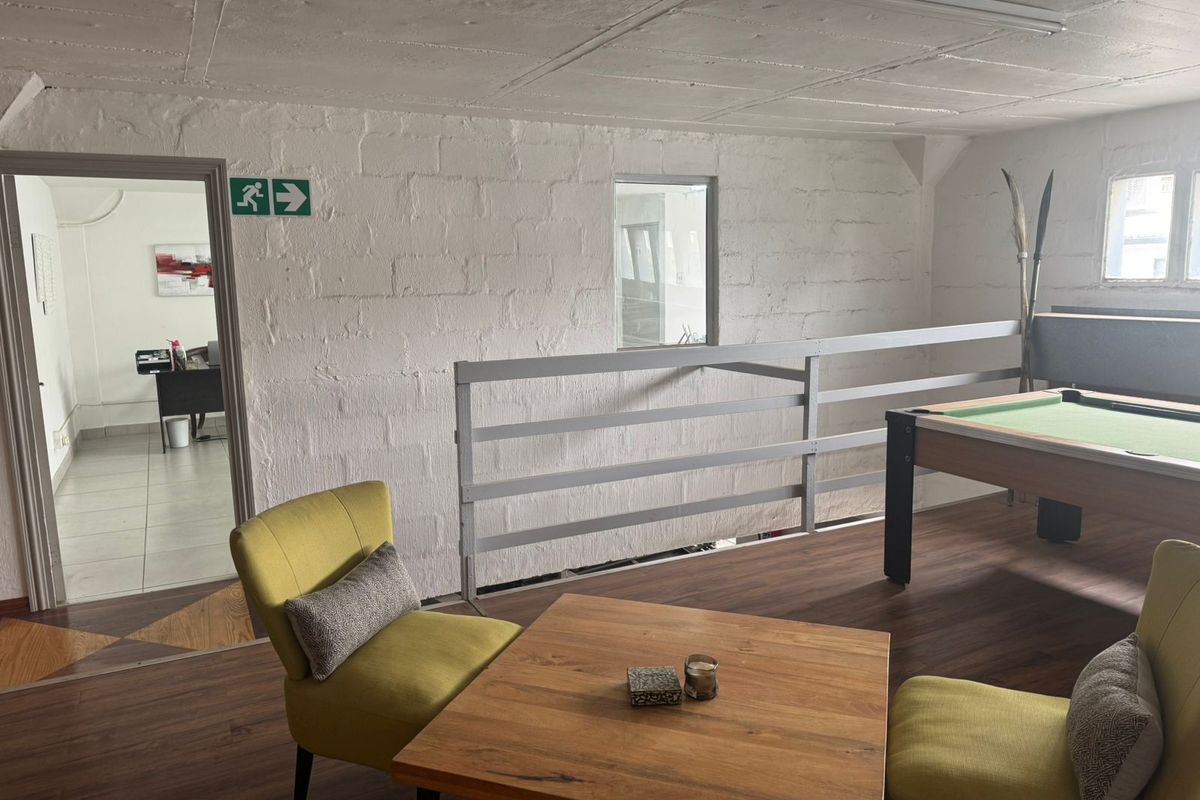 Industrial-style mezzanine living area featuring exposed concrete ceilings, painted blockwork walls, and laminate flooring with an adjacent office space.