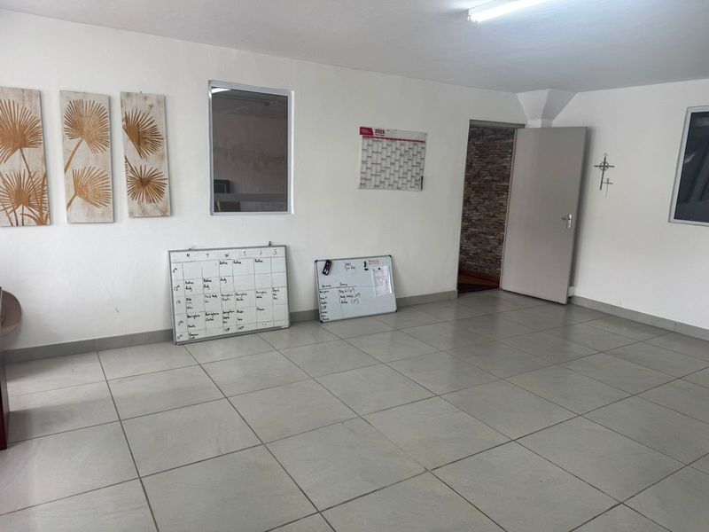 A functional office space featuring neutral tiled flooring, bright overhead lighting, and an internal window, providing a clean and versatile workspace.