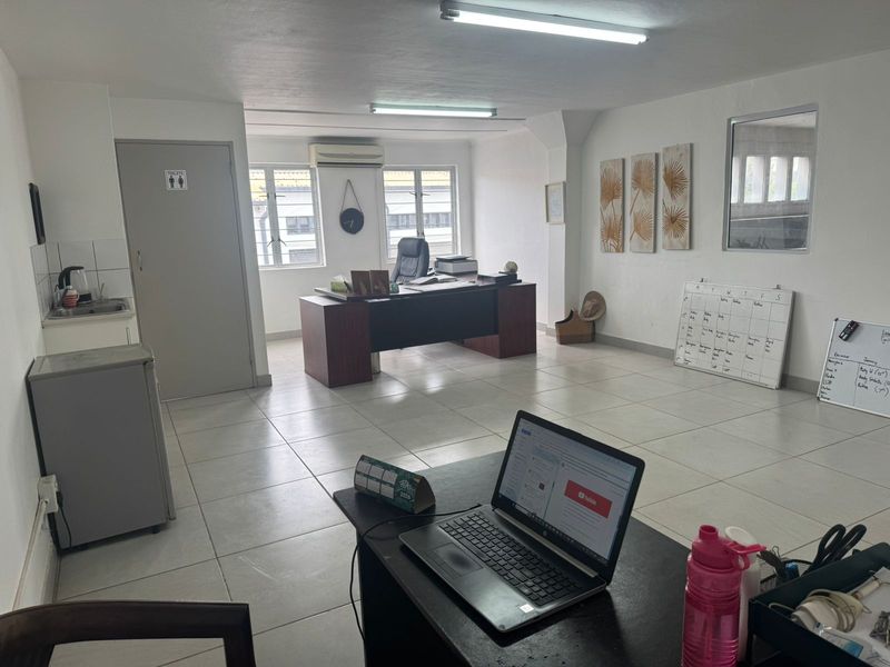 A functional office space featuring tiled flooring, built-in air conditioning, and a small kitchenette area, suitable for professional use.