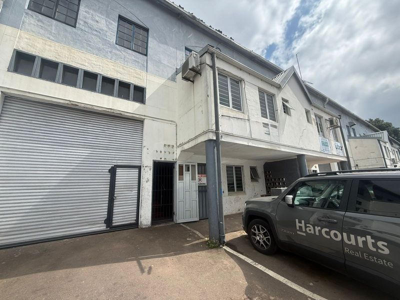 Front elevation of an industrial property featuring a large roller shutter door, security access, and multi-level facade with visible wear.