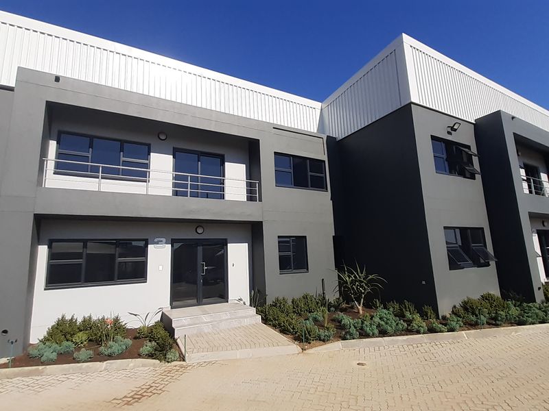 Modern industrial office or warehouse unit featuring a contemporary grey facade, metal roof cladding, aluminium windows, and a paved entrance area.