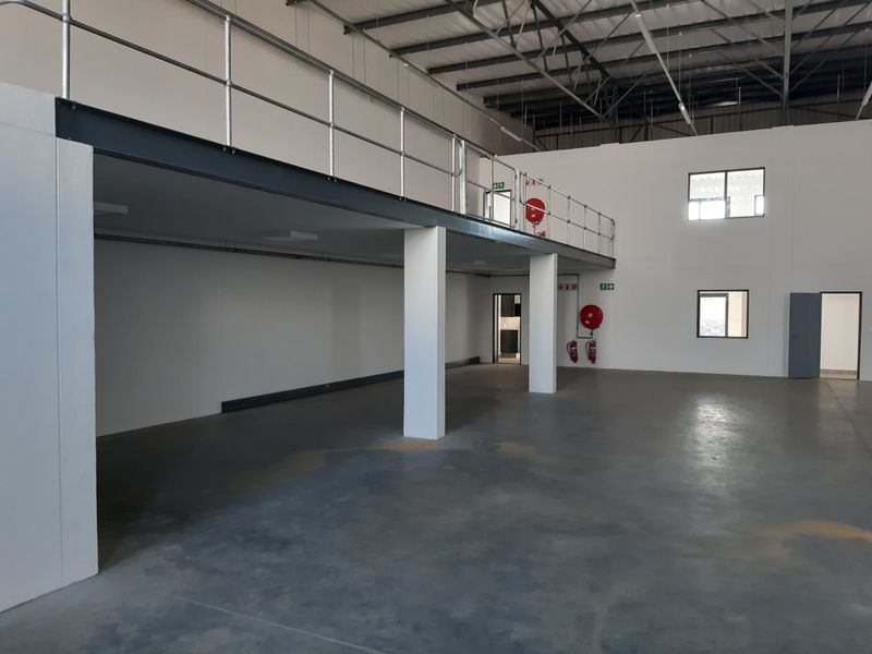 Spacious industrial warehouse unit featuring a mezzanine level, concrete flooring, and exposed steel roof structure, suitable for various commercial or storage applications.