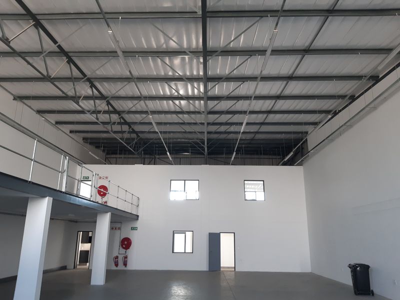 Spacious industrial warehouse unit featuring high ceilings with exposed steel trusses, a mezzanine level, and functional fire safety equipment.