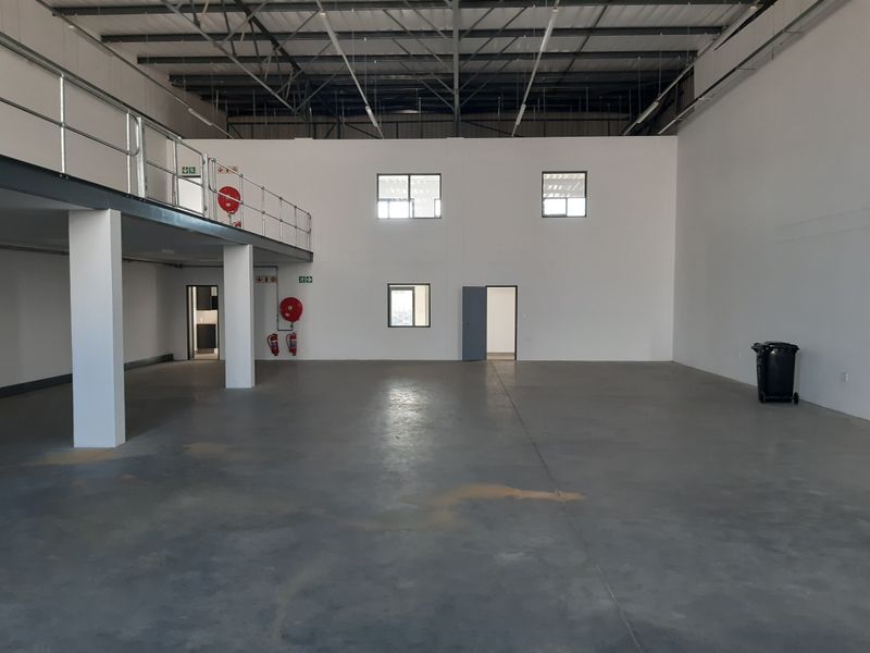 Spacious industrial warehouse unit featuring a mezzanine level, high ceilings with exposed steel trusses, polished concrete flooring, and integrated fire safety equipment.