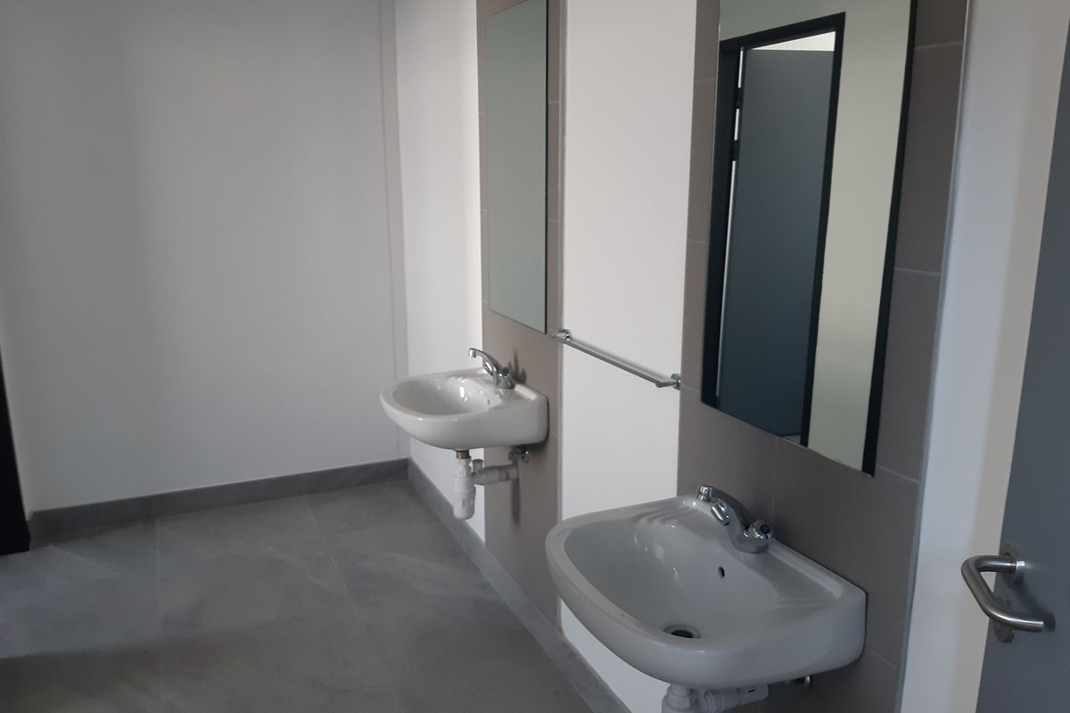 A clean, modern industrial-style bathroom featuring dual wall-mounted ceramic basins, chrome fixtures, tiled splashbacks, and large wall-mounted mirrors.