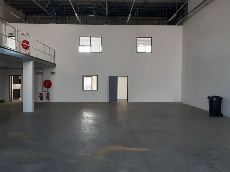 Spacious industrial warehouse unit featuring a mezzanine level, concrete flooring, and exposed steel roof structure, suitable for various commercial or storage applications.