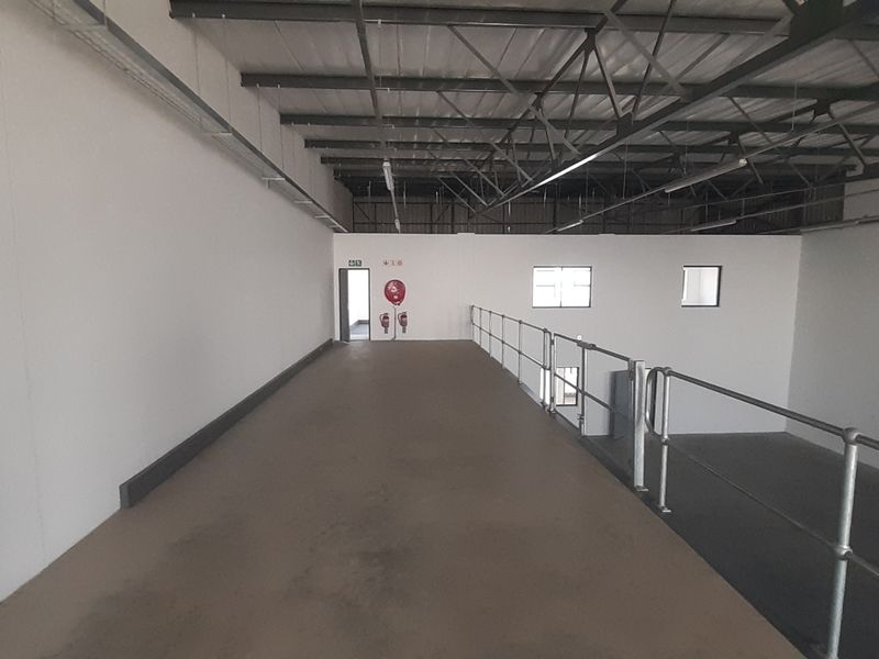 Spacious industrial mezzanine level featuring exposed steel roof trusses, safety railings, and clean white walls, suitable for storage or additional workspace.