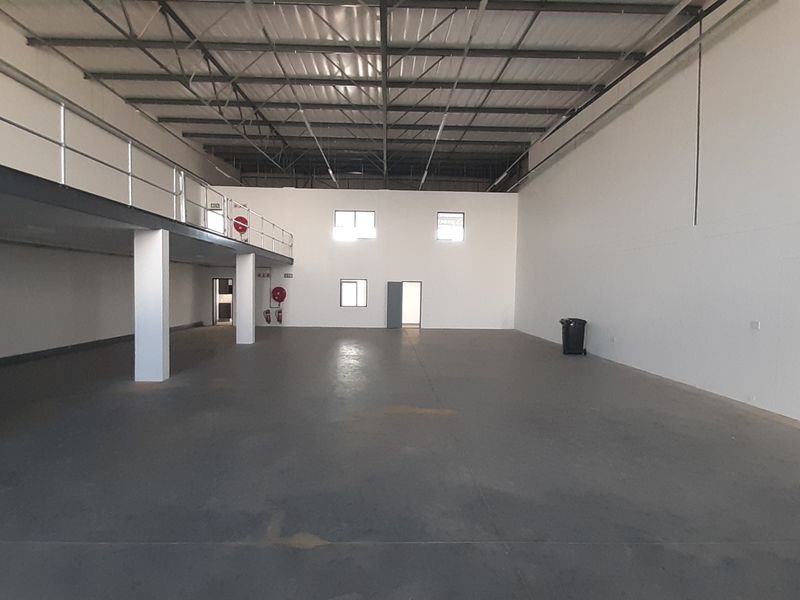 Spacious industrial warehouse unit featuring a mezzanine level, high ceilings with exposed steel trusses, and durable concrete flooring.
