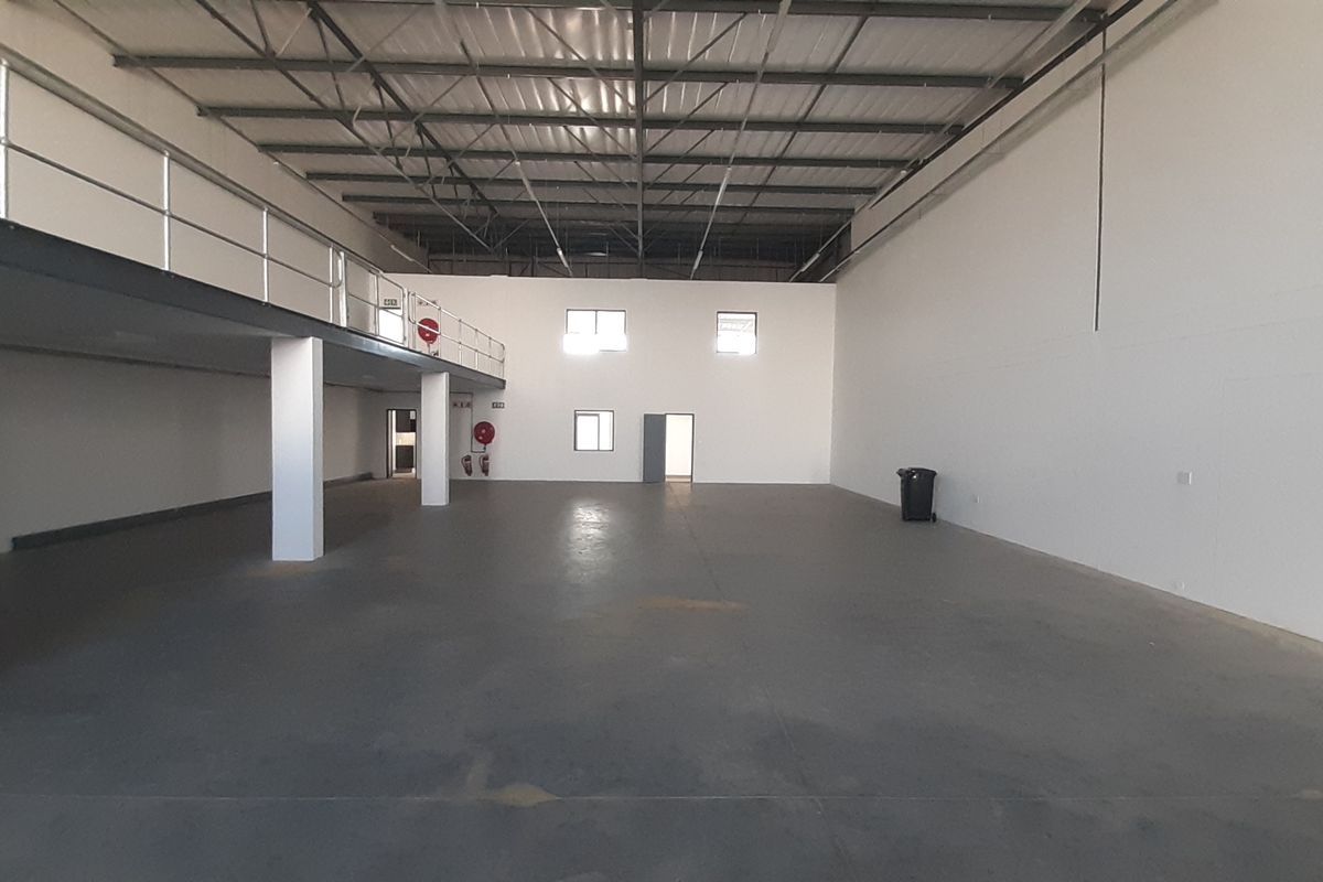 Spacious industrial warehouse unit featuring a mezzanine level, high ceilings with exposed steel trusses, and durable concrete flooring.