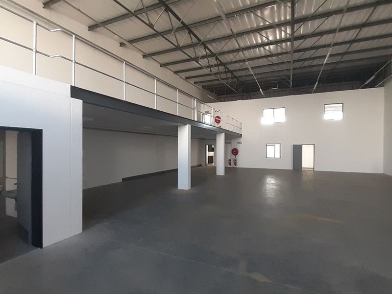 Spacious industrial warehouse unit featuring a mezzanine level, exposed steel roof trusses, concrete flooring, and integrated safety railings.