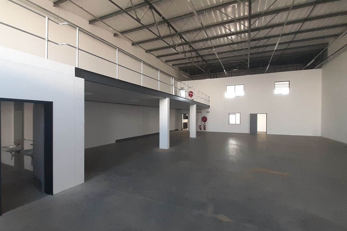 Spacious industrial warehouse unit featuring a mezzanine level, exposed steel roof trusses, concrete flooring, and integrated safety railings.