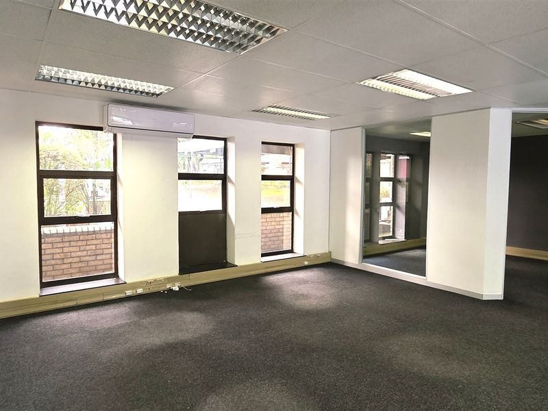 An empty, open-plan office space featuring recessed lighting, split-system air conditioning, carpeted flooring, and large windows providing natural light.
