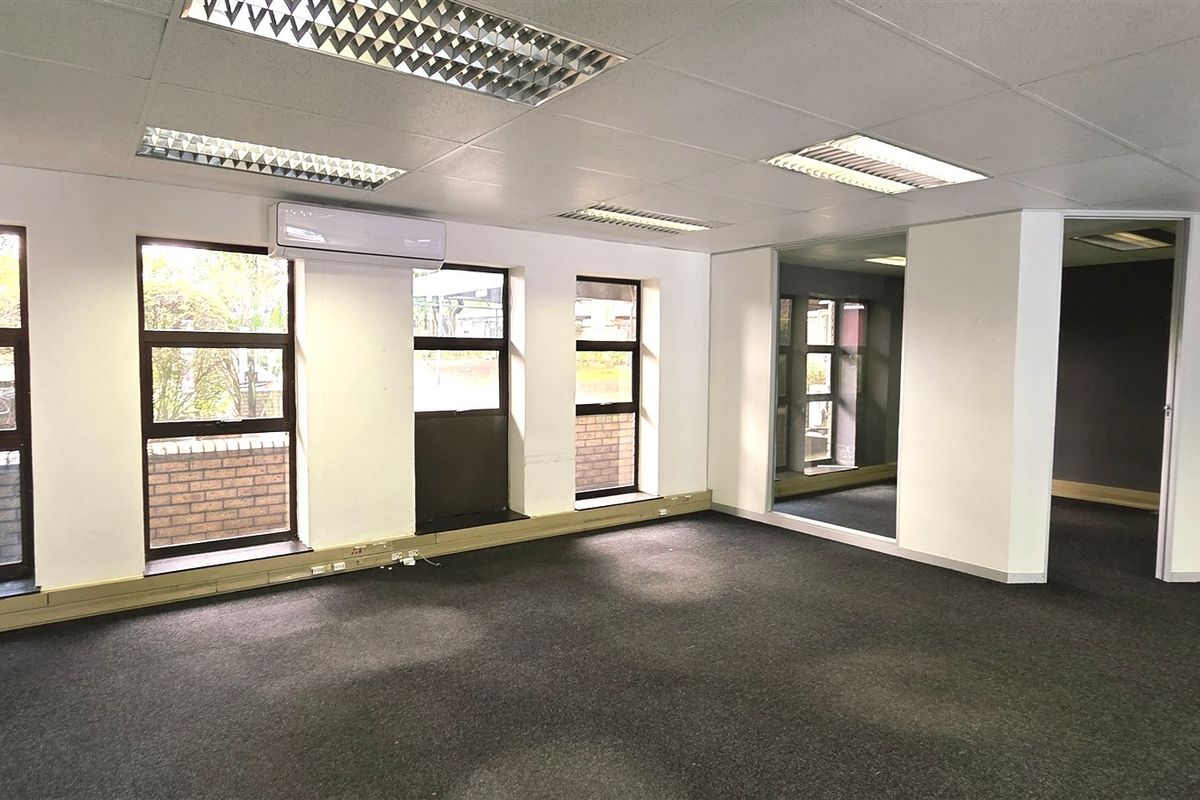 An empty, open-plan office space featuring recessed lighting, split-system air conditioning, carpeted flooring, and large windows providing natural light.