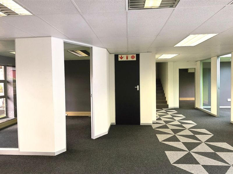 A vacant, modern office space featuring glass partitioning, suspended ceilings with recessed lighting, and patterned carpet flooring throughout the open-plan layout.