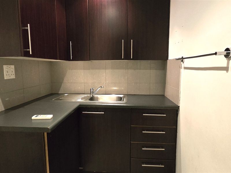A compact kitchenette featuring dark wood cabinetry, a stainless steel sink, and a tiled backsplash, suitable for an office break area.