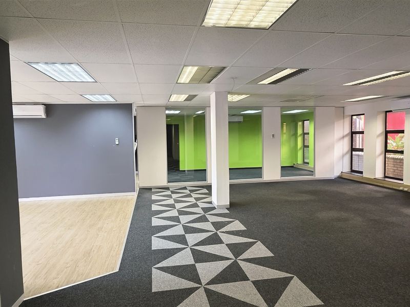 Spacious open-plan office area featuring a mix of carpet and laminate flooring, glass partitioning, and integrated air conditioning units.