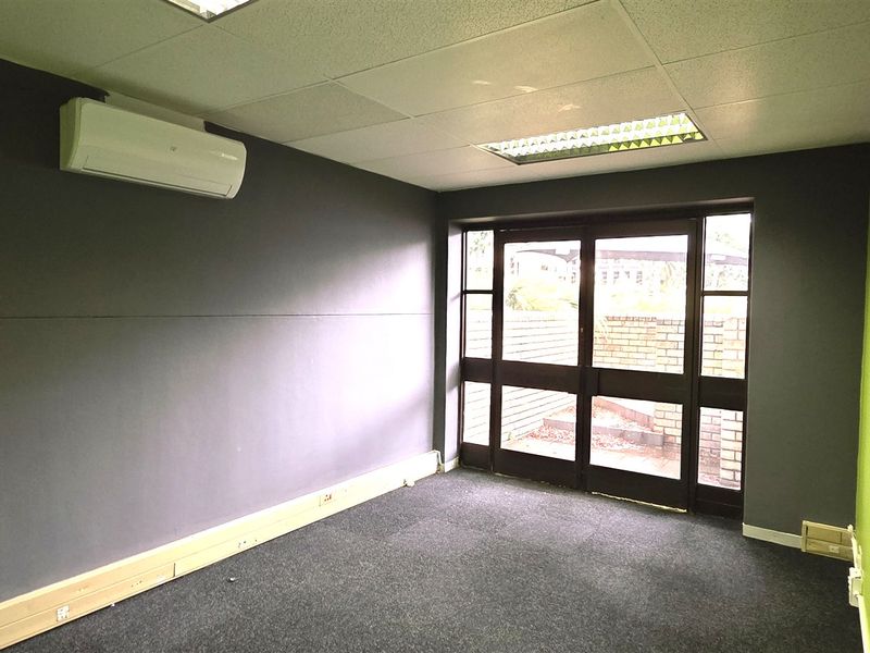 A vacant office space featuring dark grey and lime green walls, carpet flooring, a split-system air conditioner, and a glass-paneled door leading outside.
