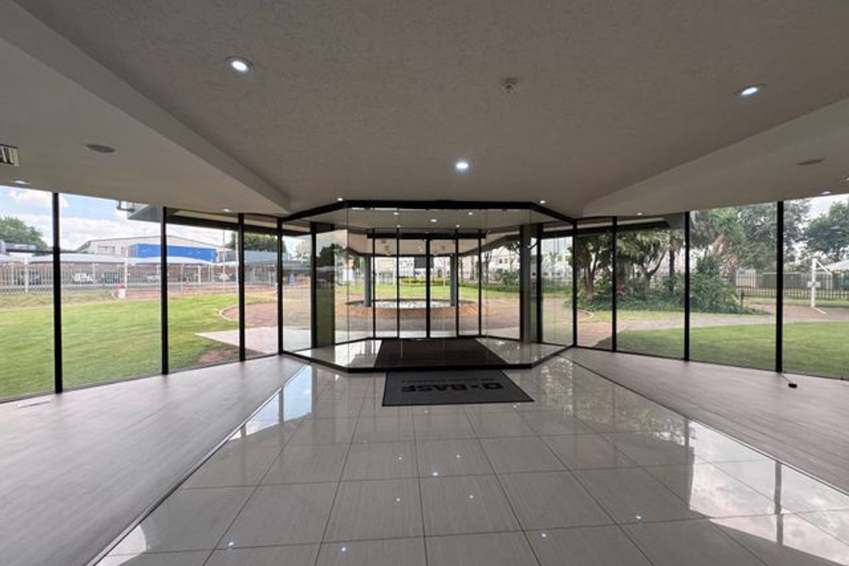 Spacious modern entrance lobby featuring extensive floor-to-ceiling glass walls, polished tiled flooring, and recessed lighting, offering clear views of the surrounding industrial grounds.