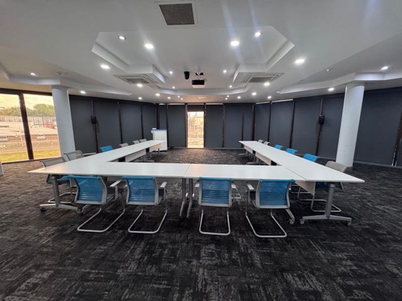 A professional office or boardroom space featuring recessed ceiling lighting, central air conditioning, and large windows with dark roller blinds.