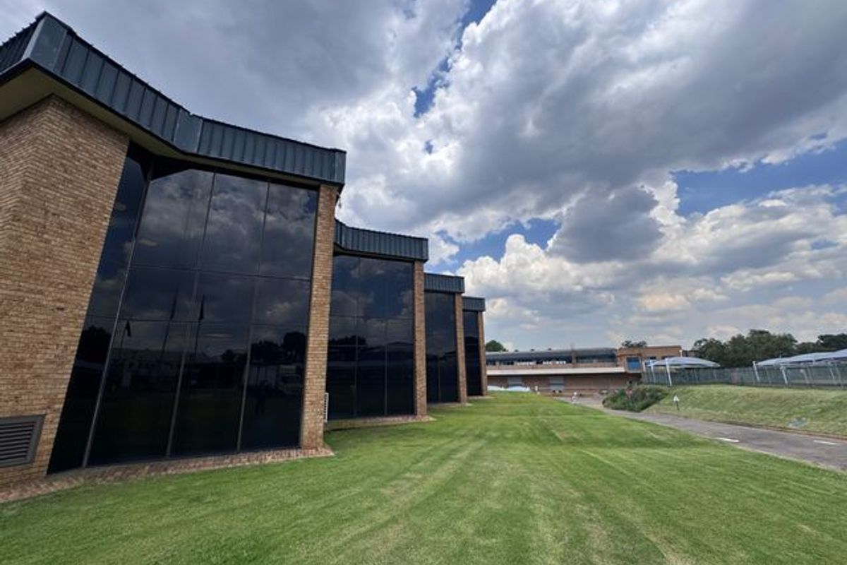 Exterior view of an industrial building featuring a brick facade with extensive tinted glass curtain walling and surrounding landscaped lawn area.