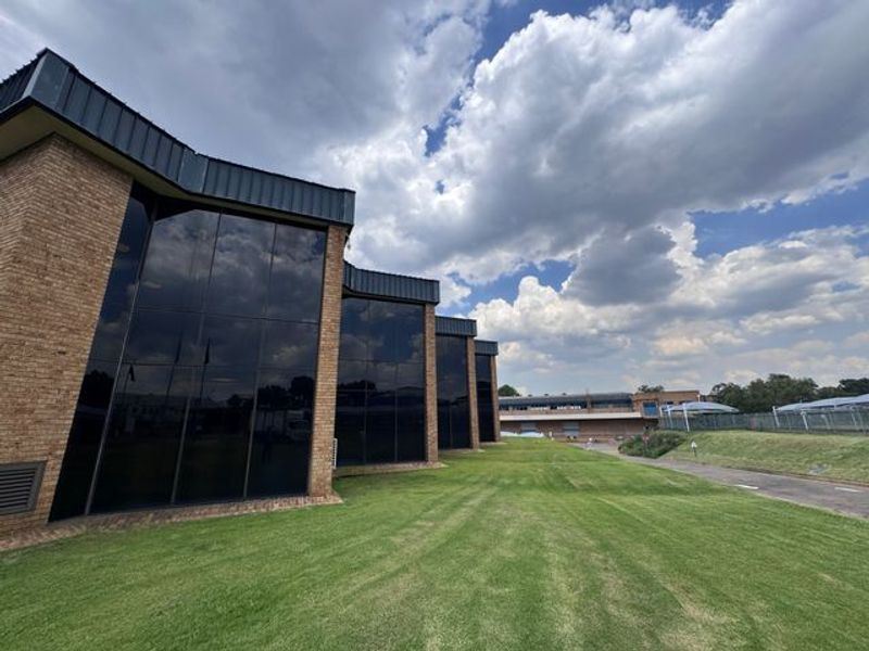 Exterior view of an industrial building featuring a brick facade with extensive tinted glass curtain walling and surrounding landscaped lawn area.