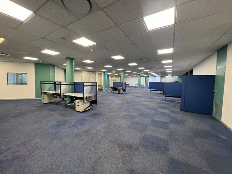 Spacious open-plan industrial office area featuring suspended ceilings, recessed lighting, and modular carpet flooring with existing built-in workstation partitions.