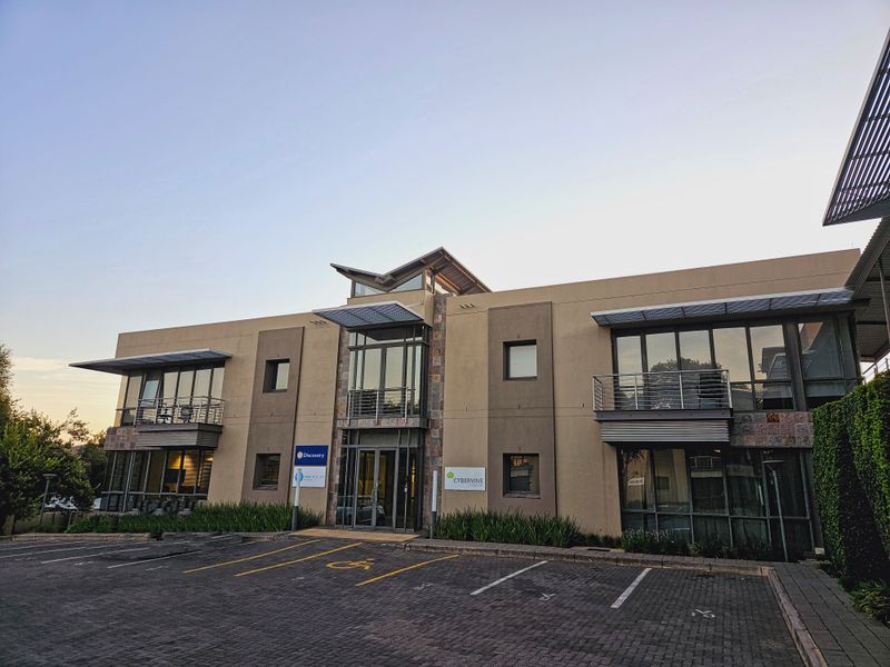 Modern two-story office building featuring a glass facade, stone accents, metal awnings, and dedicated paved parking with accessible bays.