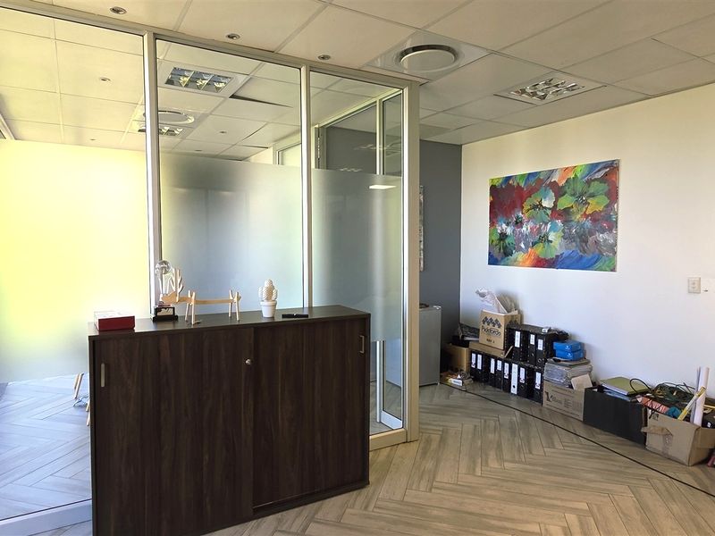 A professional office space featuring modern glass partitions, a suspended ceiling with recessed lighting, and stylish herringbone flooring.