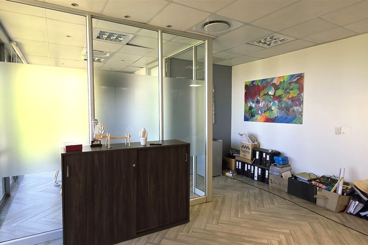 A professional office space featuring modern glass partitions, a suspended ceiling with recessed lighting, and stylish herringbone flooring.