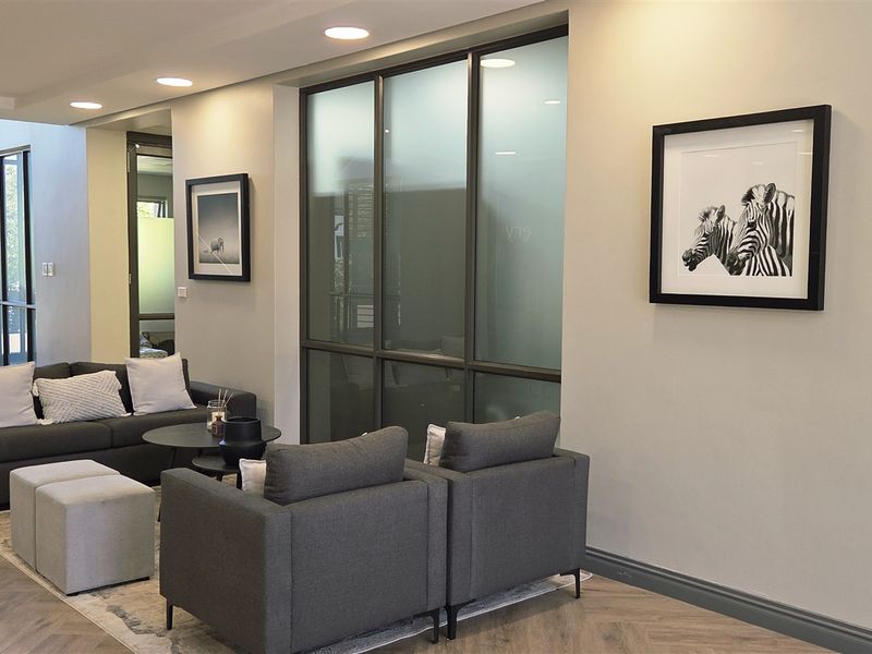 Modern office reception area featuring herringbone flooring, recessed lighting, and glass partition walls with a staircase leading to the upper level.