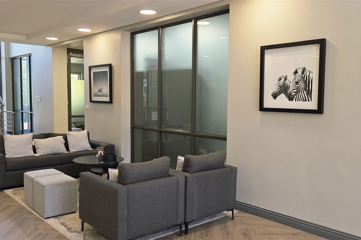Modern office reception area featuring herringbone flooring, recessed lighting, and glass partition walls with a staircase leading to the upper level.