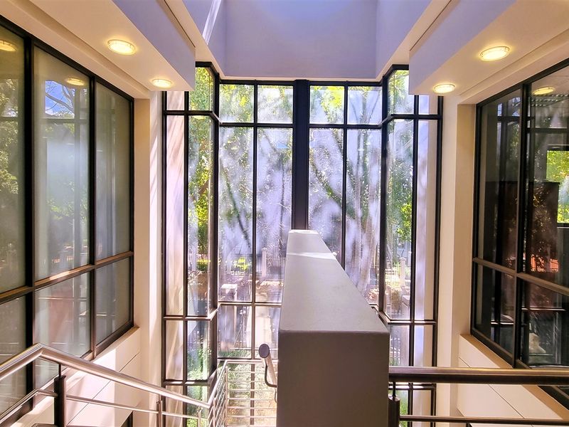 A bright, modern office entrance featuring a dramatic full-height glass curtain wall, a central staircase with stainless steel handrails, and abundant natural light.
