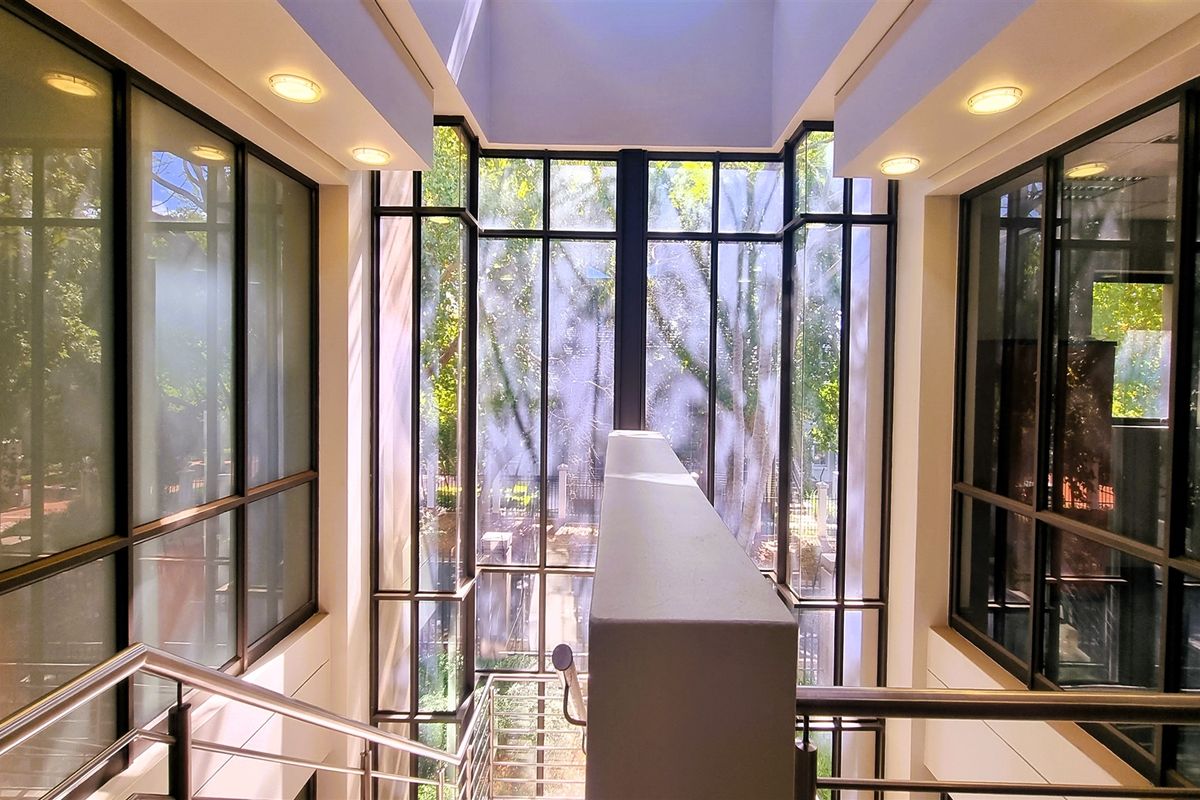A bright, modern office entrance featuring a dramatic full-height glass curtain wall, a central staircase with stainless steel handrails, and abundant natural light.