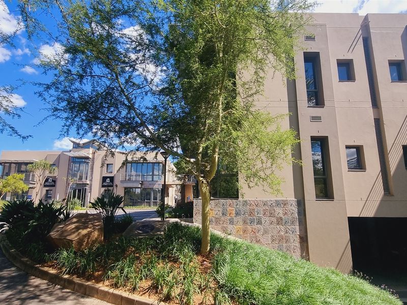 Modern office building exterior featuring stone cladding, landscaped garden areas, and paved access, showcasing a professional and well-maintained commercial property facade.