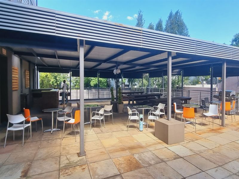 Spacious covered outdoor patio area featuring paved flooring, a metal roof structure, and a built-in brick counter, ideal for office break-out space.