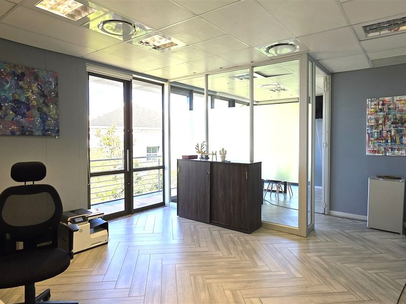 Modern office space featuring herringbone tile flooring, a glass partition wall, and a sliding door leading to a small balcony.