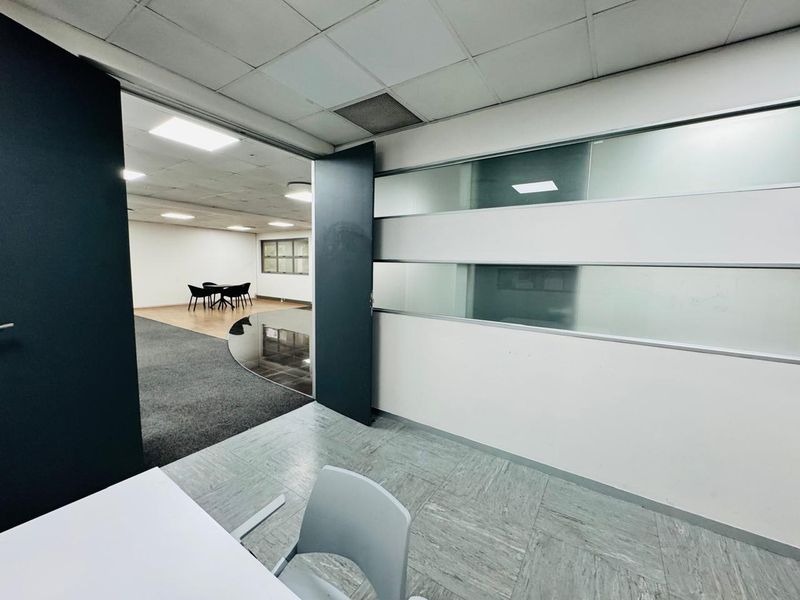 A professional office space featuring a glass partition wall, suspended ceiling with recessed lighting, and a combination of vinyl and carpet flooring.