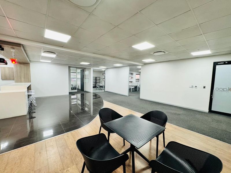 Modern open-plan office space featuring a mix of tiled and carpeted flooring, recessed ceiling lights, and glass partitions for a professional work environment.