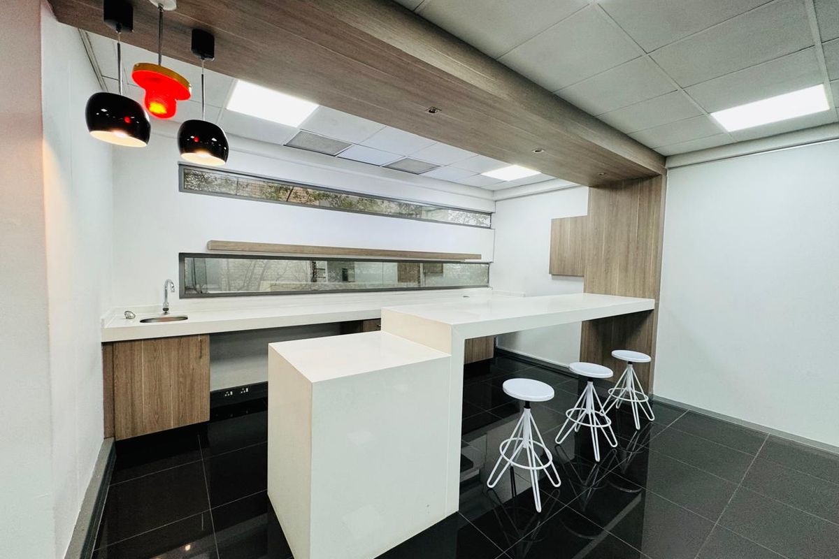 Modern office kitchenette featuring sleek cabinetry, stone countertops, integrated sink, and contemporary lighting, set against a polished dark tiled floor.