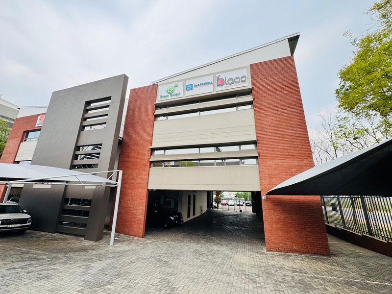 Modern multi-story office building featuring a brick facade, paved driveway, and integrated covered parking area with professional commercial signage.