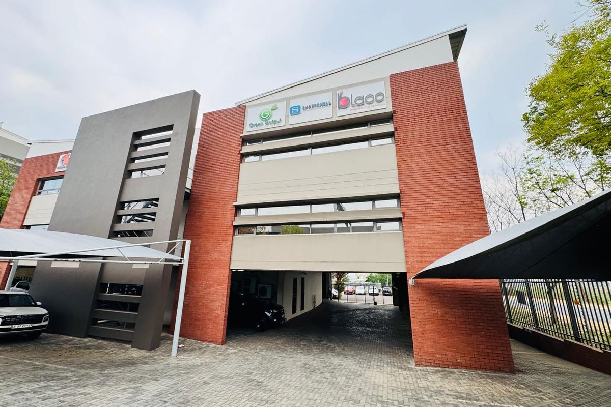 Modern multi-story office building featuring a brick facade, paved driveway, and integrated covered parking area with professional commercial signage.