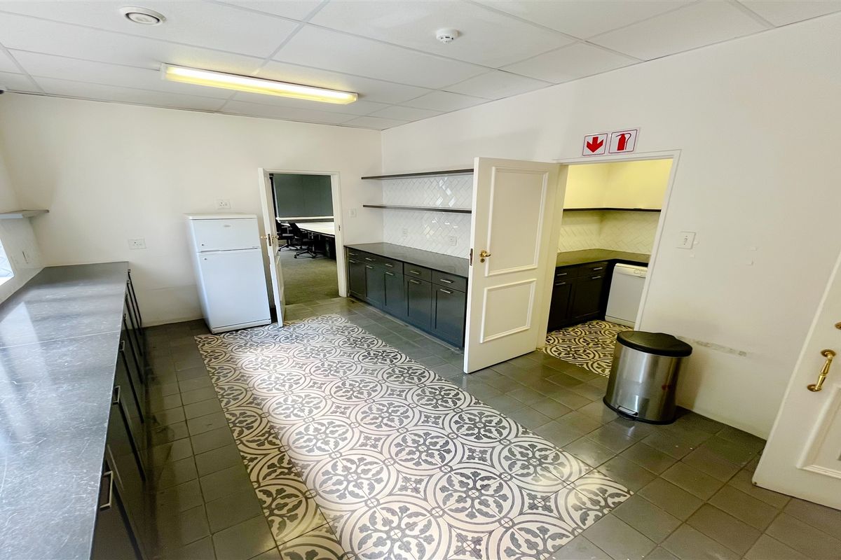 A functional office kitchen area featuring built-in cabinetry, laminate countertops, a tiled backsplash, and a distinctive patterned floor design.
