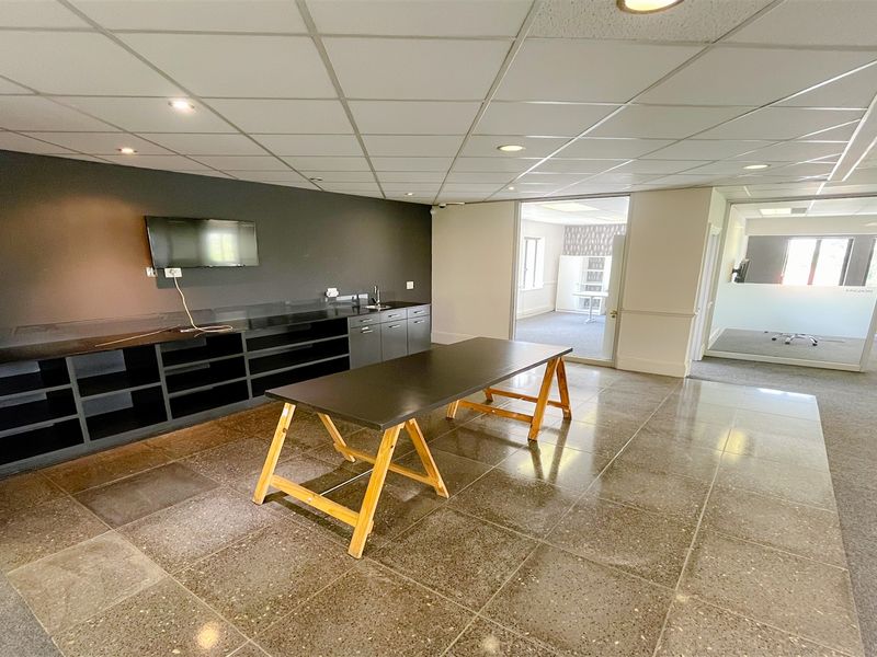 Modern office space featuring built-in cabinetry with integrated sink, glass partition walls, and durable tiled flooring with recessed lighting.