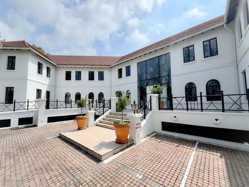 A well-maintained office building exterior featuring a paved parking area, central entrance steps, and a prominent glass facade with classic architectural detailing.