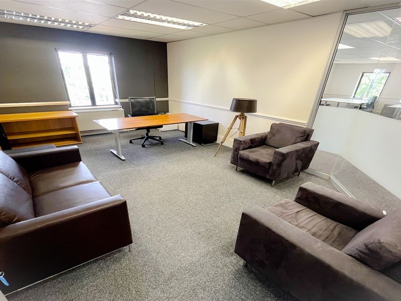 A professional office space featuring carpeted flooring, a suspended ceiling with recessed lighting, and a glass partition wall providing a bright, modern work environment.